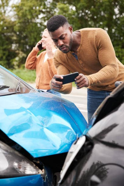 Driver photographing front-end collision damage with a smartphone at the roadside